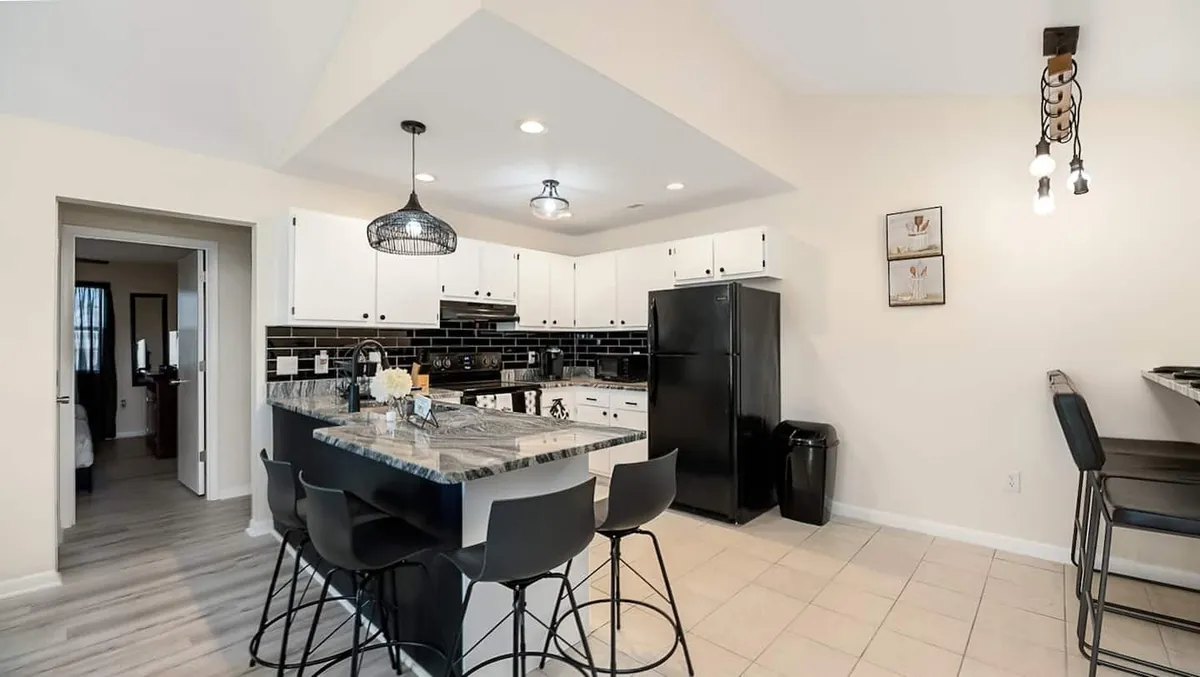 A modern kitchen featuring a spacious island with sleek black and white cabinetry, comfortable bar stools, and stylish pendant lighting. The open layout offers clear sightlines to adjacent living and dining areas, emphasizing both functionality and a social atmosphere.
