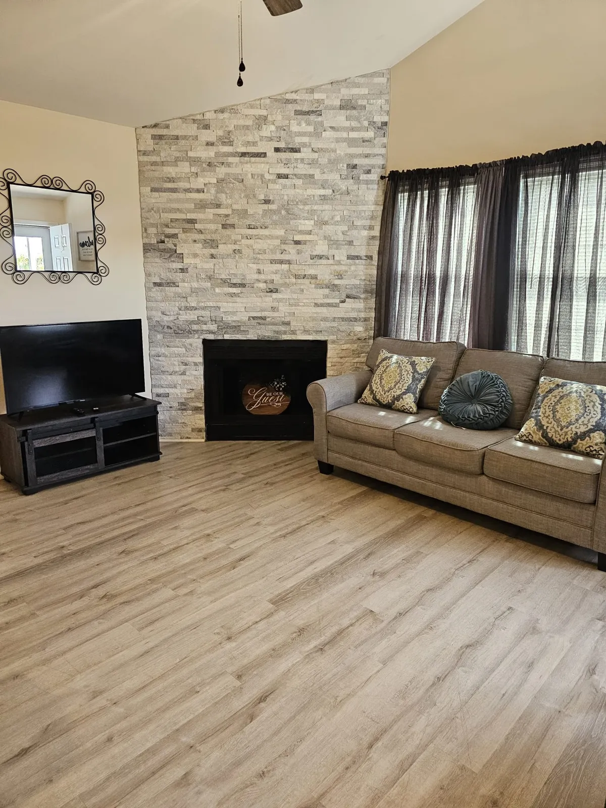 A cozy family room with a stone accent wall housing a modern fireplace, a comfortable sofa adorned with decorative pillows, a sleek TV unit, and ambient lighting. The space exudes warmth and is ideal for both relaxation and social gatherings.