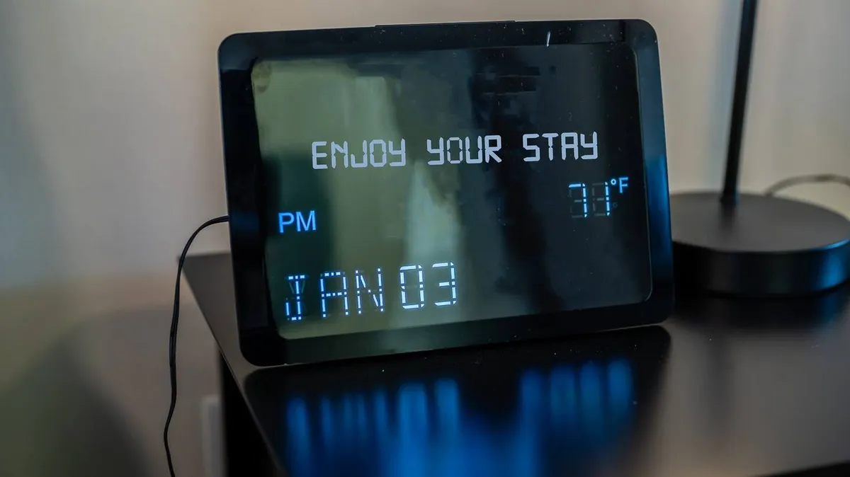 A cozy interior corner with a digital clock and a table lamp on a wooden surface, suggesting a space for planning daily activities or unwinding after a city excursion. The inviting mood and practical setup hint at mornings spent preparing for new explorations or evenings reflecting on the day.