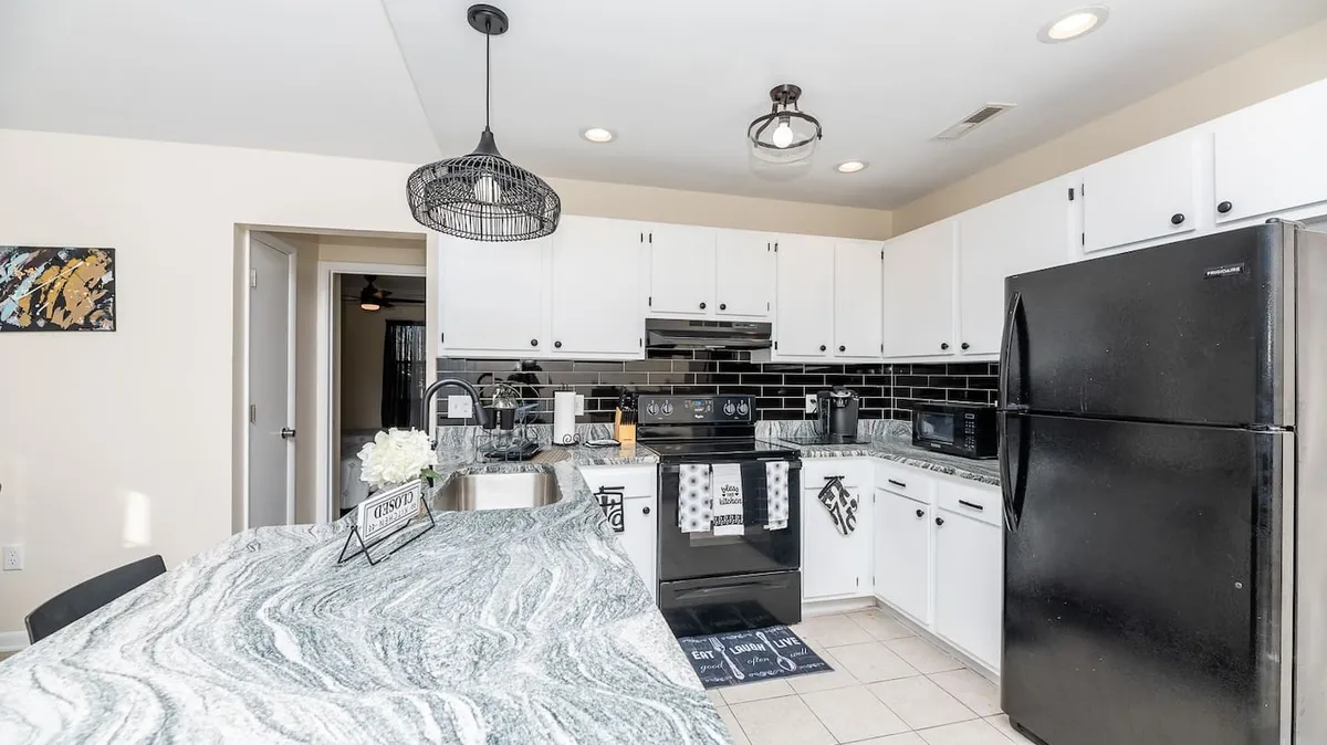 A contemporary kitchen scene with marble countertops, stainless steel and black appliances, and elegant pendant lighting. The backsplash tiles add a touch of sophistication, and the space feels ready for cooking, entertaining, or family meals.