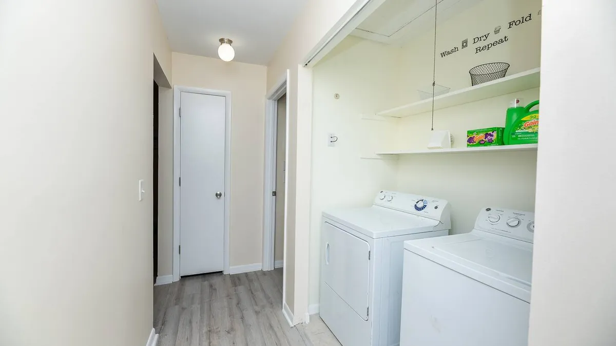 A tidy laundry area equipped with a washing machine, dryer, and shelving for storage. The space looks practical, organized, and efficient—ideal for managing everyday needs during a short-term stay.
