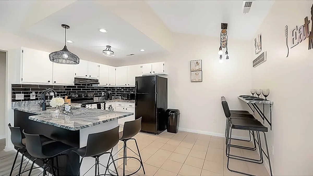 A modern kitchen with an island countertop, black refrigerator, bar stools, and decorative wall art. The layout is ideal for cooking, entertaining, and gathering for meals, creating a welcoming and functional hub for family activities.